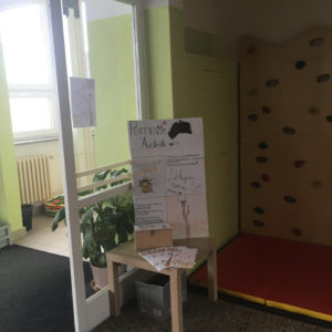 Pohled na vestibul školy s plakátem, letáky a kasičkou